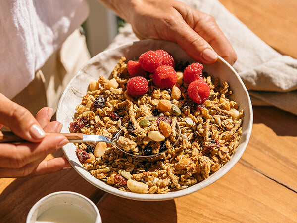 Brookfarm Macadamia Muesli with Rasberries in a bowl held by a woman with linen on table